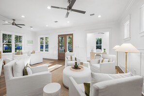 A spacious living room with white furniture, a ceiling fan, and large windows.