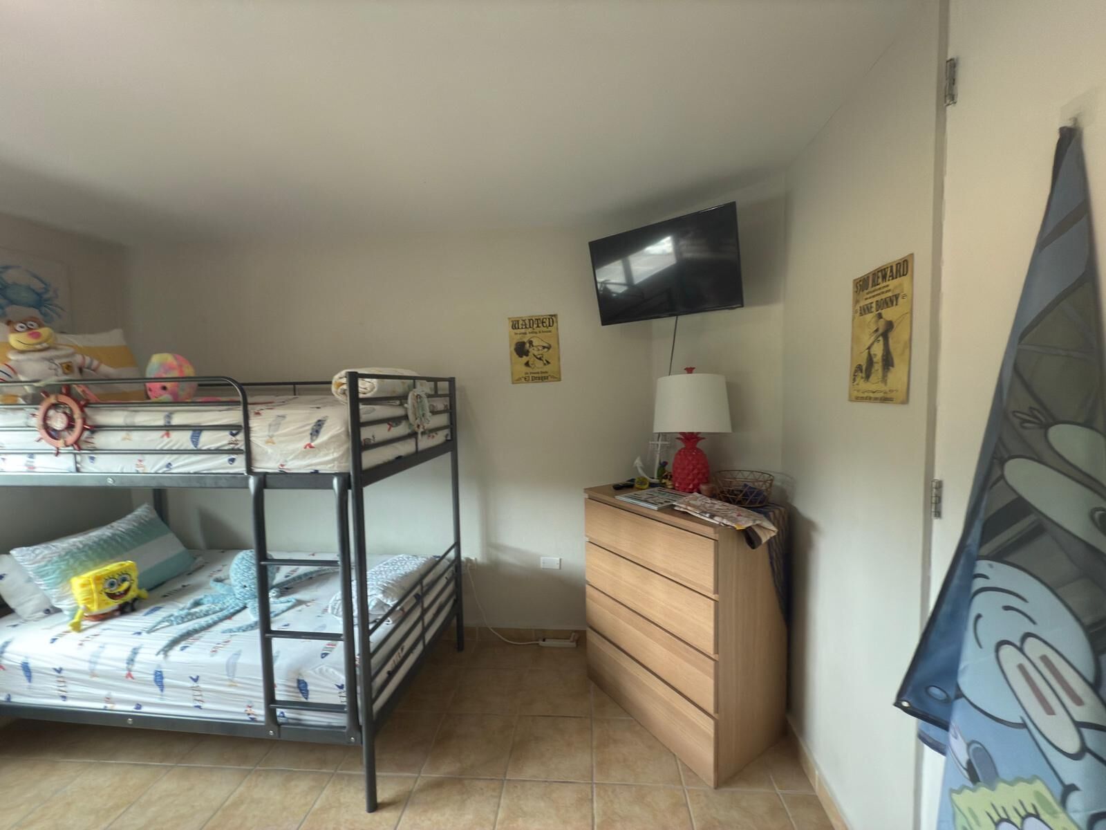 A bunk bed with toys, a wooden dresser, a television, and cartoon posters on the wall.