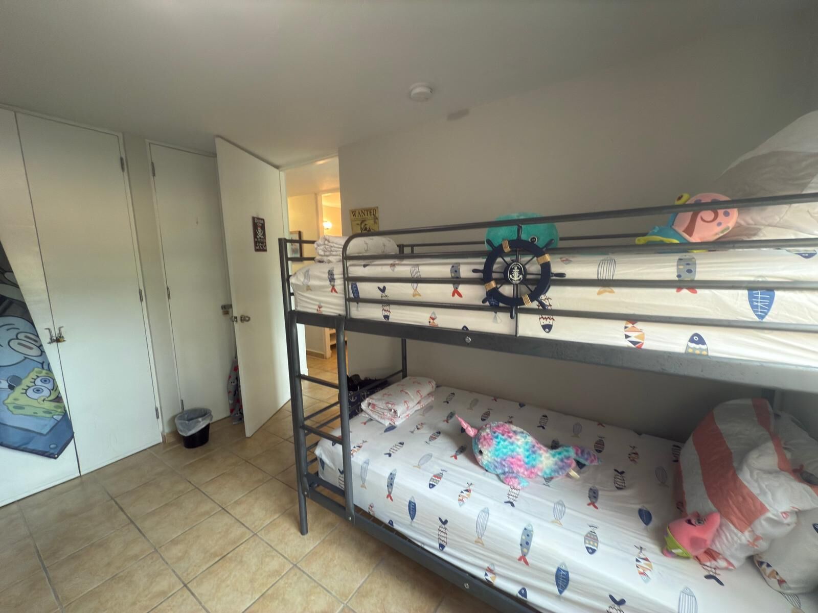 Camera con letto a castello, una porta, un cestino e un poster appeso al muro.
