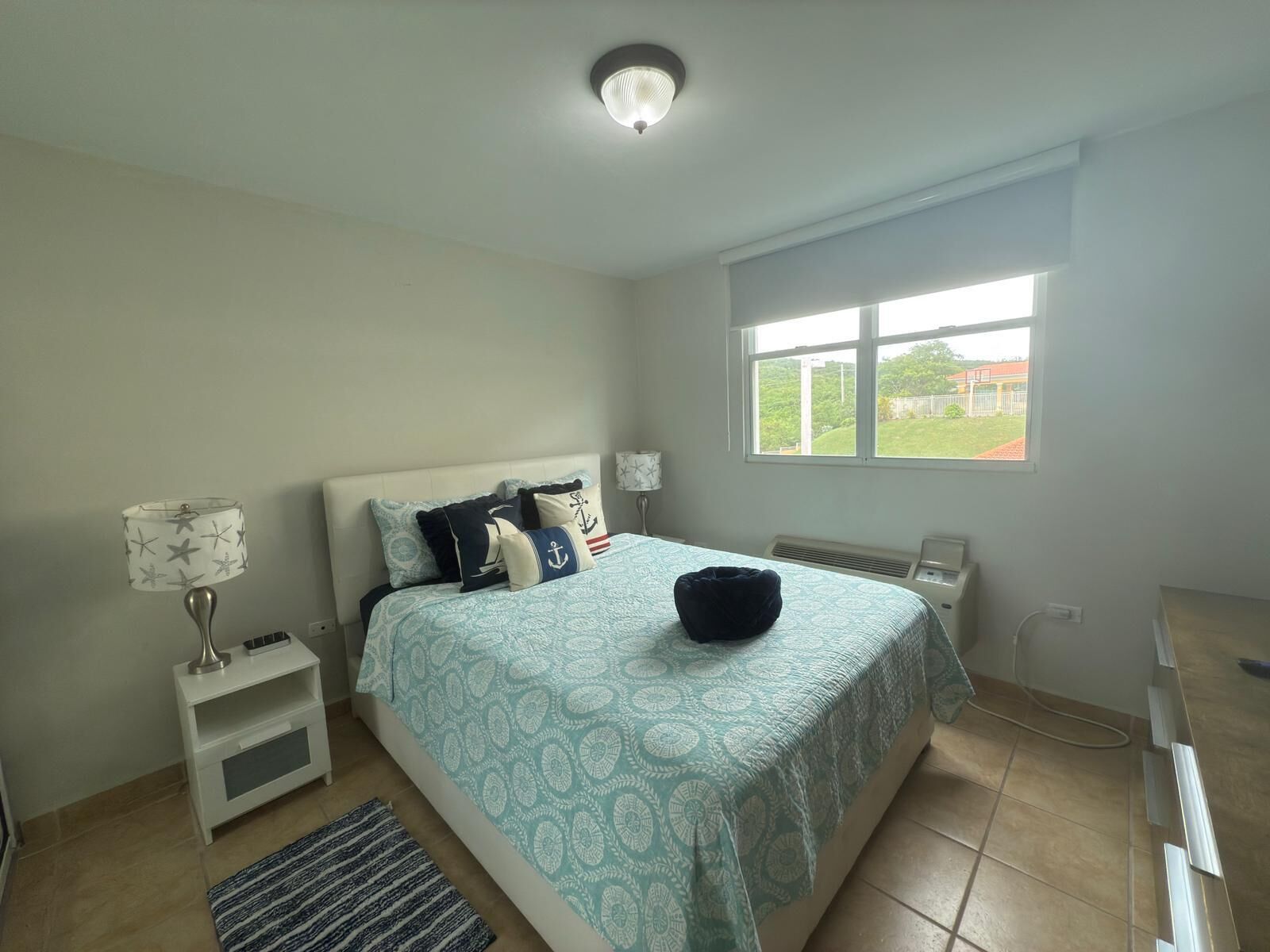 A bedroom with a bed, a nightstand, a lamp, a window, and a radiator.
