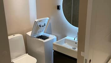 A compact bathroom with a toilet, a washing machine, and a sink.