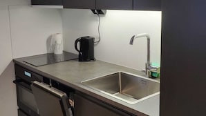Une cuisine moderne avec des meubles de couleur sombre, un évier en acier inoxydable et une machine à café.