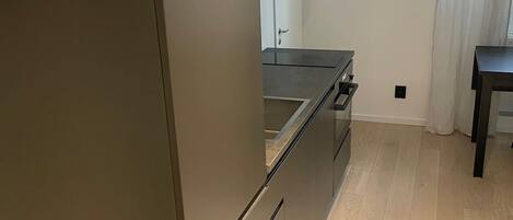 A modern kitchen with a dark-colored refrigerator, a built-in oven, and a wooden countertop.