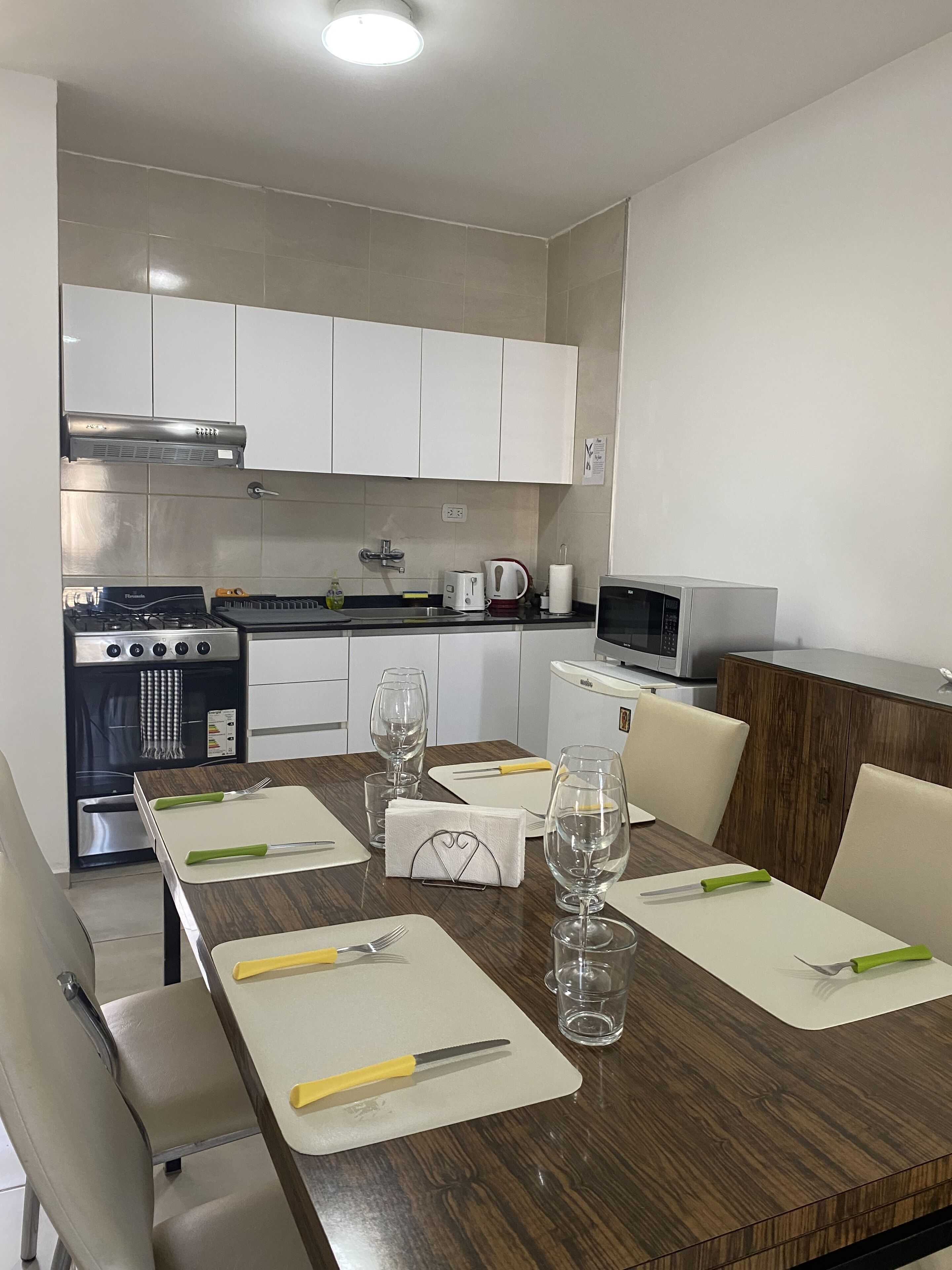 Une cuisine moderne avec des meubles blancs, une cuisinière, un four à micro-ondes et une table à manger, le tout agrémenté de couverts et de verres.