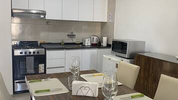 Une cuisine moderne avec des meubles blancs, une cuisinière, un four à micro-ondes et une table à manger, le tout agrémenté de couverts et de verres.