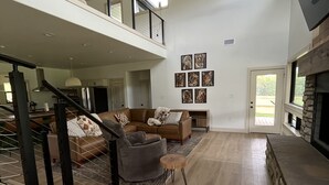 Amplia sala de estar con techo alto, chimenea y escalera que conduce a un nivel superior.