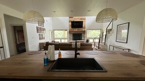 Una cocina moderna con una isla central, dos lámparas colgantes y una chimenea de piedra.