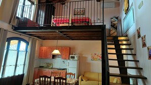 A loft-style apartment with a kitchen, dining area, and a balcony with a red bed. - Apartment Flowers La Burraia (GAMBASSI TERME)