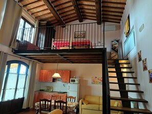 A loft-style apartment with a kitchen, dining area, and a balcony with a red bed.