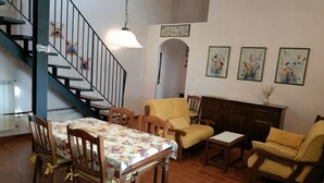 A dining area with a table and chairs, a staircase, and a living room with a sofa and armchairs. - Apartment Flowers La Burraia (GAMBASSI TERME)
