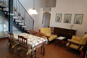 A dining area with a table and chairs, a staircase, and a living room with a sofa and armchairs.