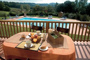 A table set with breakfast items, a pool, and a view of the countryside.