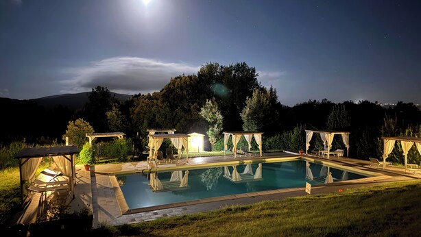 A swimming pool with a pergola and lounge chairs, surrounded by grass and trees, under a night sky with a visible moon. - Apartment Flowers La Burraia (GAMBASSI TERME)