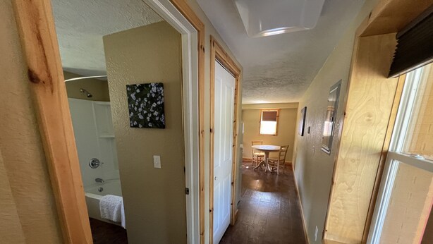 A hallway with wooden floors, a dining area with a table and chairs, and a bathroom with a shower.