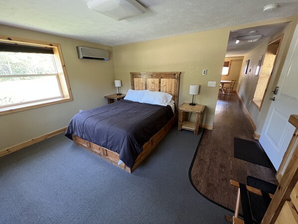 Een slaapkamer met een houten bed, nachtkastje, lamp en raam.