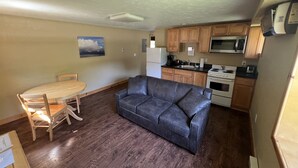 A compact living space with a kitchenette, a dining area with a table and chairs, and a gray sofa.