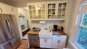 A kitchen with white cabinets, a stainless steel refrigerator, a wooden countertop, and a window with a view of trees.