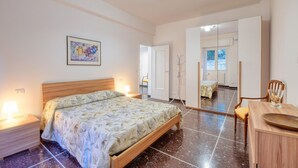Een slaapkamer met een bed, bedlampen, een houten nachtkastje, een spiegel en uitzicht op een balkon.
