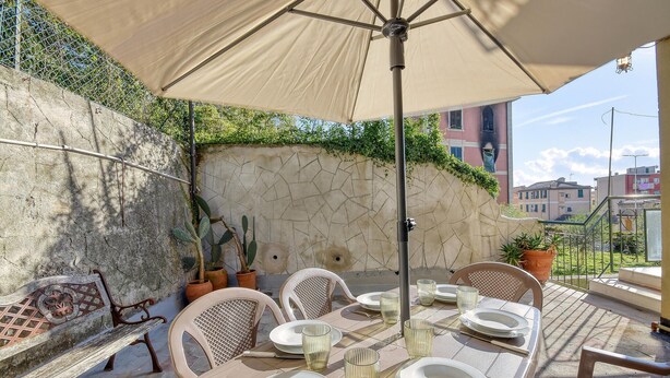 Een buitenterras met een tafel voor vier personen, omringd door stoelen, onder een grote parasol.