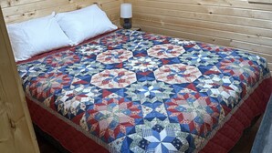 A wooden cabin room with a bed, white pillows, a red and blue quilt, and a nightstand with a lamp. - Green cabin close to University of Central Missouri and Whiteman AF Base  (Warrensburg)