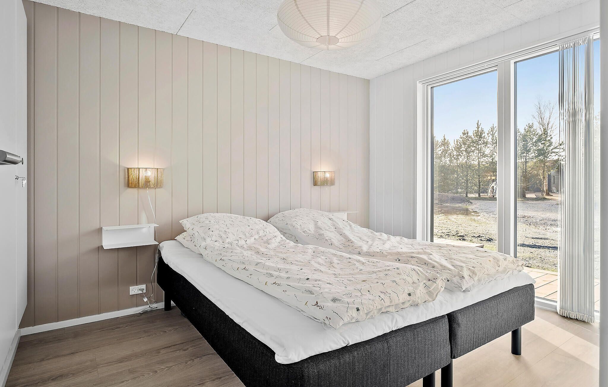 Camera da letto con un ampio letto, due lampade a parete e vista su un paesaggio naturale attraverso un'ampia porta scorrevole in vetro.
