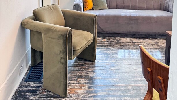 Una sala de estar moderna con un sofá gris, un sillón color beige y una silla de madera. Una lámpara de pie y un espejo están en la pared.