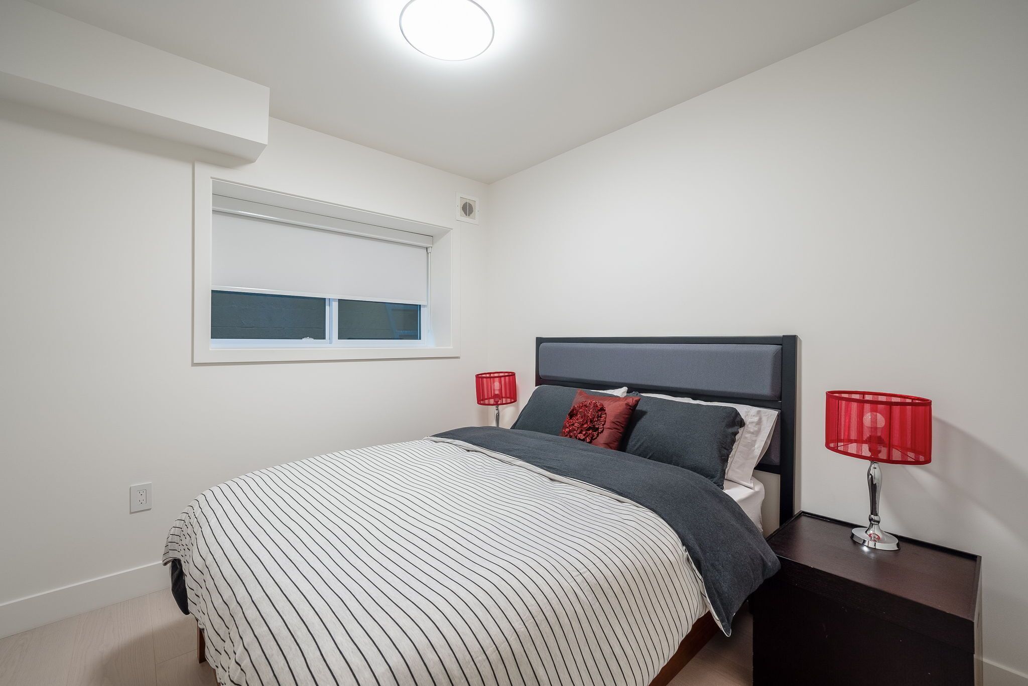 Une chambre à coucher avec un lit, des tables de chevet, une fenêtre et une lampe rouge.