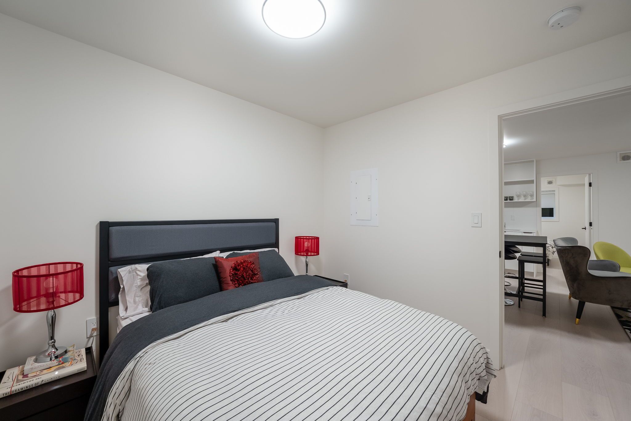 A neatly arranged bedroom with a bed, bedside lamps, a nightstand, and a desk area with a chair.