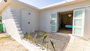 Une maison moderne à l’extérieur blanc, avec un escalier apparent et une porte donnant sur une chambre à coucher équipée d’un lit et d’un lustre.