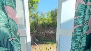 Une porte ouverte donne sur un espace dallé, d’où l’on a une vue dégagée sur les arbres et un ciel bleu.