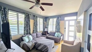 Un salon moderne avec un canapé d’angle, un petit fauteuil, un téléviseur et un ventilateur de plafond.