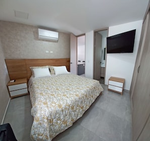 A bedroom with a bed, bedside tables, an air conditioning unit, a television, and a bathroom visible through an open door. - Serene 3-bedroom apartment with AC in charming Envigado (Envigado)