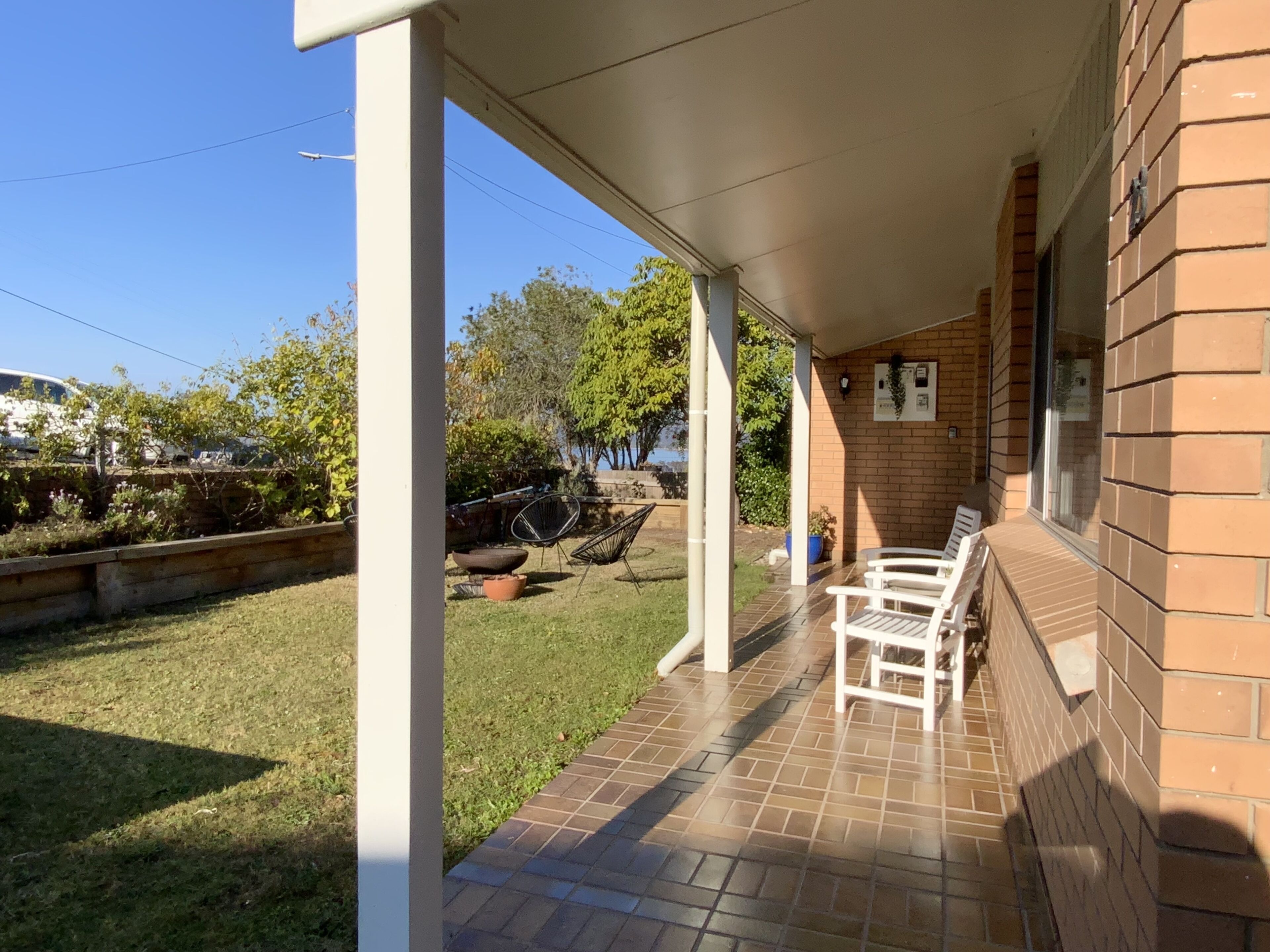A covered patio area with a brick wall, a tiled floor, and a seating area with chairs.