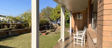 A covered patio area with a brick wall, a tiled floor, and a seating area with chairs.