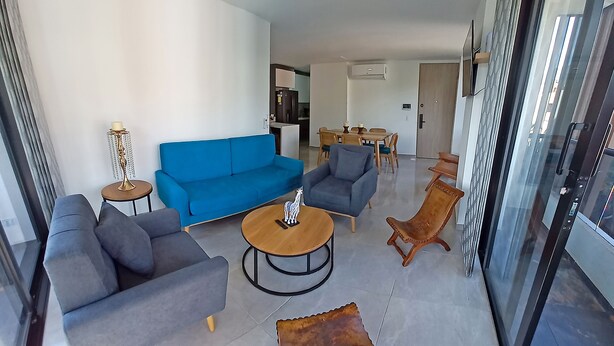 A modern living room with a blue sofa, two armchairs, a coffee table, and a glass door leading outside.
