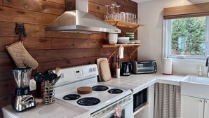Una cocina con paredes de madera, estufa, tostadora y ventana con vista a árboles.
