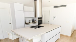Eine moderne Küche mit Kochinsel, weißen Schränken, Edelstahlgeräten und zwei Barhocker.