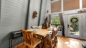 A dining area with a wooden table and chairs, a small television on a stand, and a view of the outdoors through a door. - PRIME location★Hot tub★Fire pit★Games★Sleeps 4 (Gatlinburg)