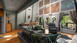 A spacious living room with a sectional sofa, a leather armchair, and a dining area with wooden furniture. - PRIME location★Hot tub★Fire pit★Games★Sleeps 4 (Gatlinburg)