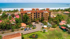 A hotel with multiple buildings, a parking area, and a beach view. - Beachfront Luxury Condo with Direct Access to the Beach, 3 BR, 2 Baths, Balcony! (Jacó)