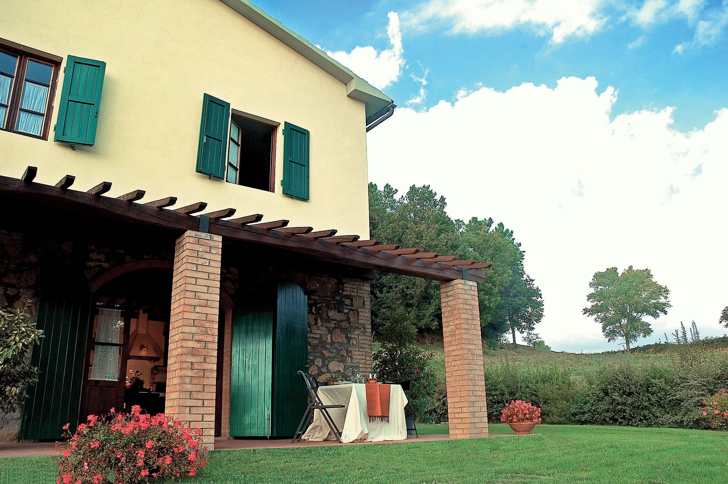 A two-story building with a stone facade, green shutters, and a covered patio area.