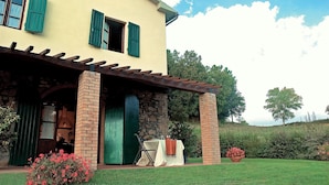 A two-story building with a stone facade, green shutters, and a covered patio area.