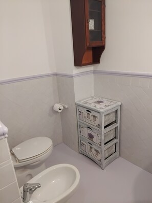 Une salle de bain équipée de toilettes, d’un bidet et d’un petit meuble de rangement avec des paniers.