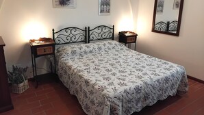 A bedroom with a bed, two bedside tables, a nightstand, a wall-mounted mirror, and two wall-mounted pictures.