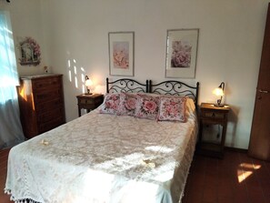 Une chambre à coucher comprenant un lit, deux tables de chevet avec des lampes, une commode et deux tableaux accrochés au mur.