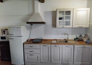 Une cuisine avec des meubles blancs, un four Ă micro-ondes, un rĂ©frigĂ©rateur, un Ă©vier et une fenĂȘtre situĂ©e au-dessus des meubles.
