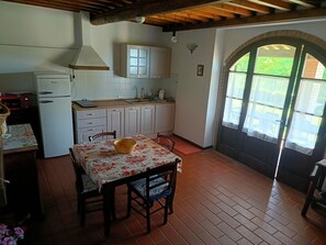 Une cuisine avec des meubles blancs, un Ă©vier et une table recouverte dâune nappe Ă motifs floraux.