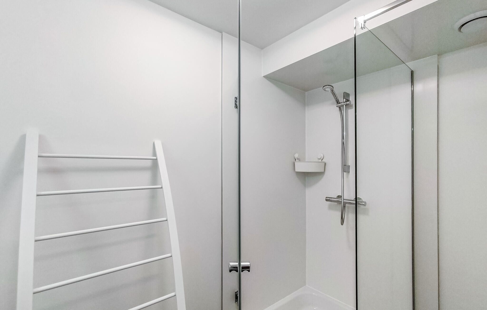A modern shower with a glass door, a white towel rack, and a small shelf with toiletries.