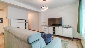 A modern living room with a sofa, a flat-screen TV, and a kitchenette area. - 1 bedroom awesome apartment in Oostende (Oostende)