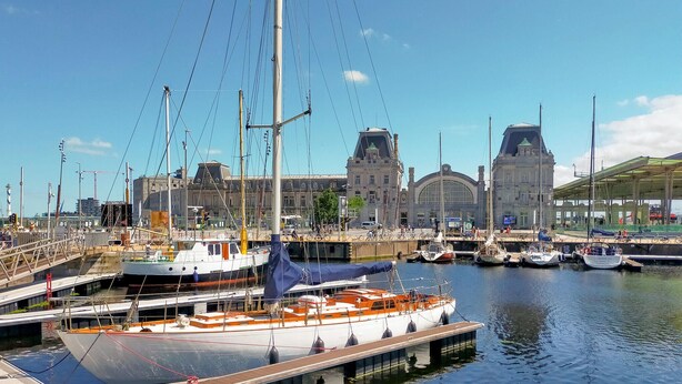 A marina with boats docked, a large building with a clock tower, and a covered area with a green roof. - 1 bedroom awesome apartment in Oostende (Oostende)